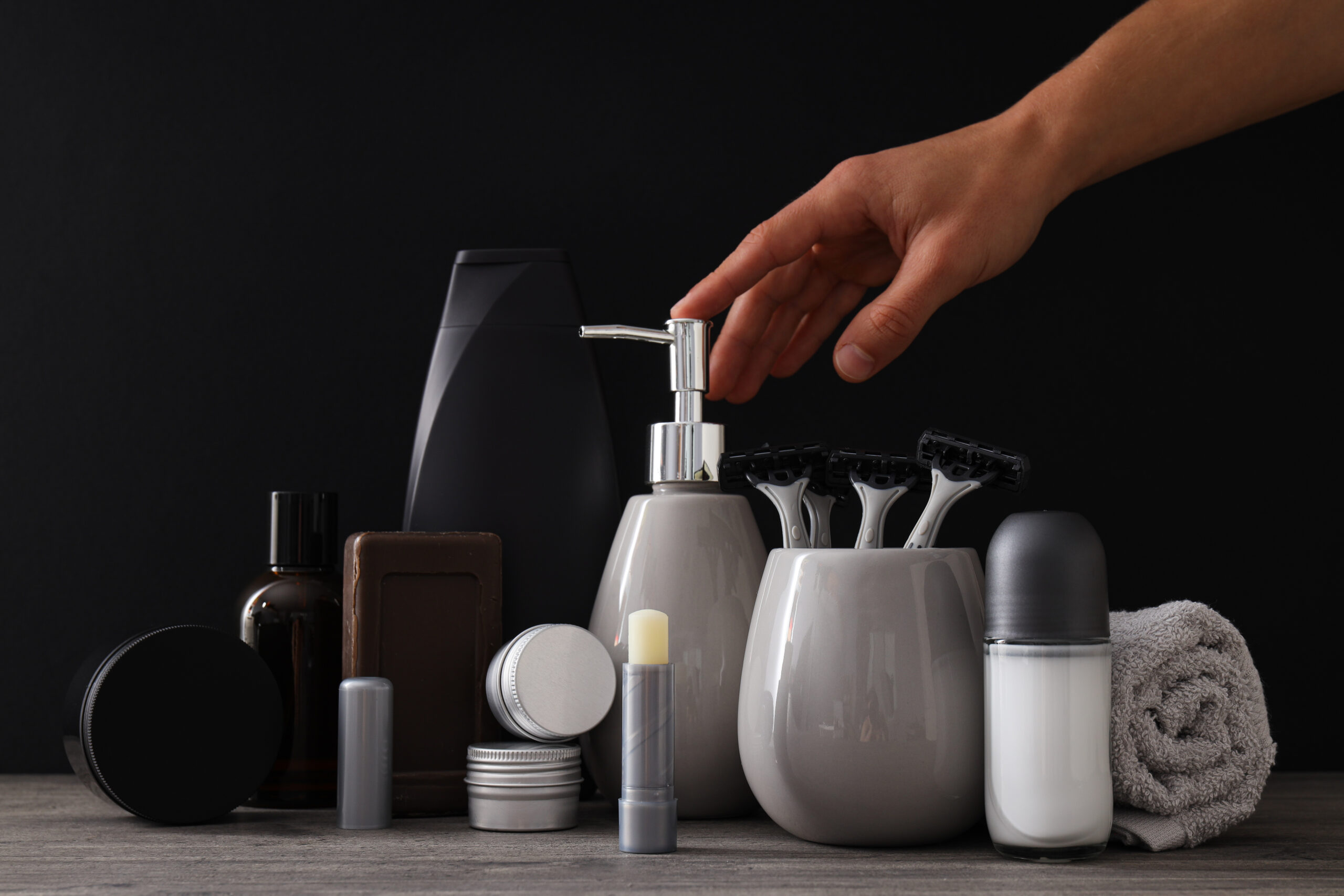 Business bottles and jars with men's cosmetics, towel and hand on black b